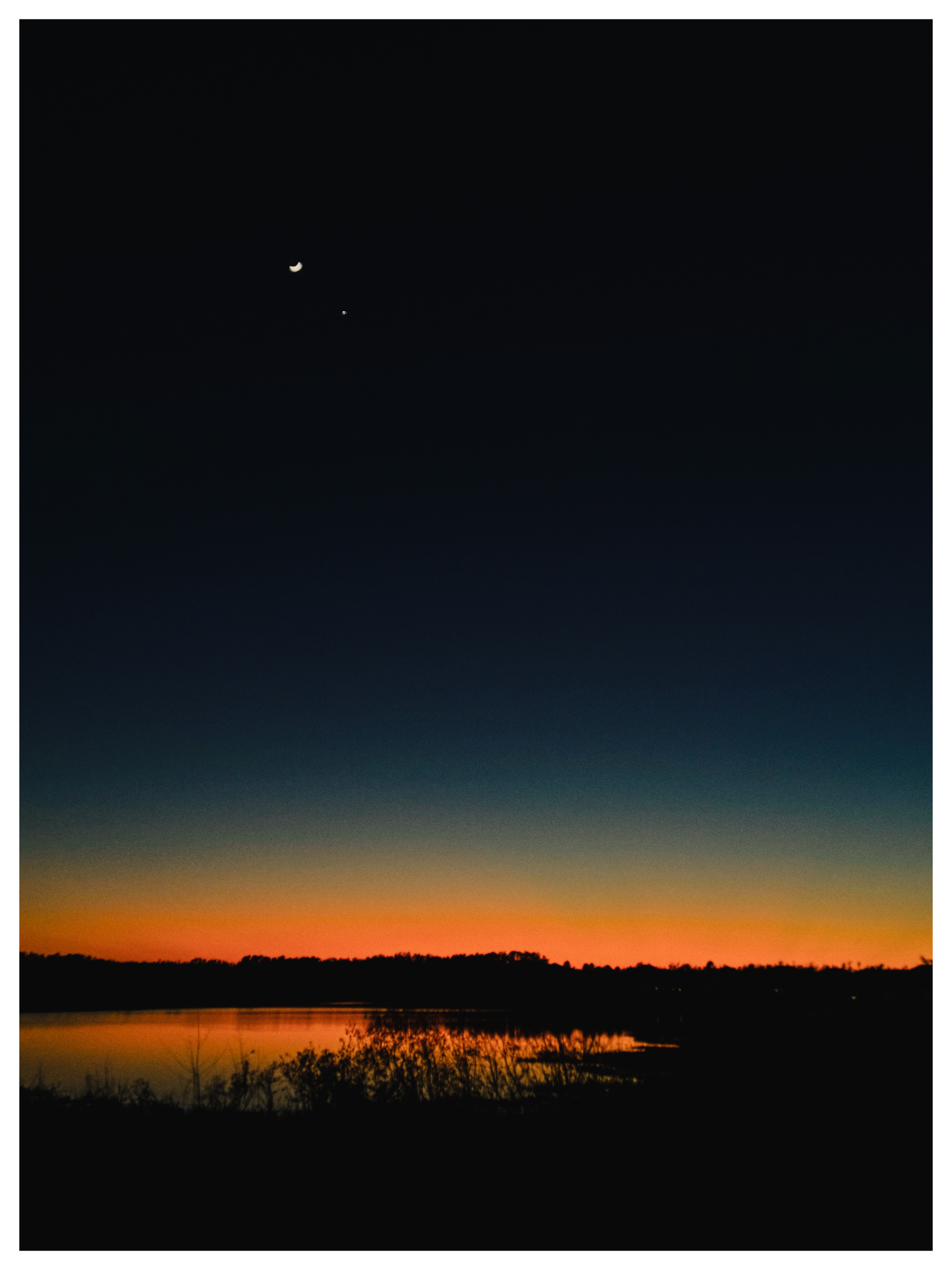 Crescent moon over a lake at dusk